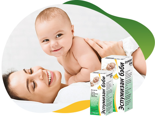 Two packs of Espumisan 100 mg/ml Emulsion in different sizes in the foreground, behind the big package is an illustrated lion. In the background there is a happy baby that lies on his smiling mother and looking curiously at the camera
